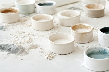 An art studio with scattered canvases, pastel chalks, and acrylic paints, creating a sense of creative chaos and inspiration. Ceramic bowls scattered on a dusty workbench, surrounded by powdered clay