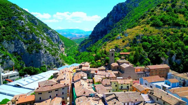Charming aerial pullback shot from Pioraco encompassing the variously colored town's buildings coming into view and a sumptuous backdrop of the Sibillini mountains ridges and gorges topped by greenery