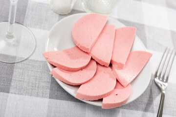 Dining table is covered with checkered tablecloth and served for lunch. Sliced boiled sausage is served for meals, cutlery and spices are served