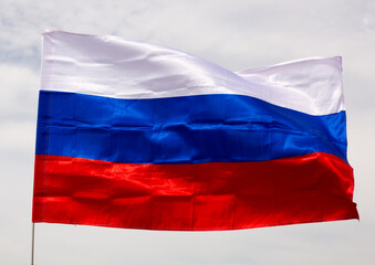 Russian tricolor flag waving in wind against sky. Russian flag on blue sky background.