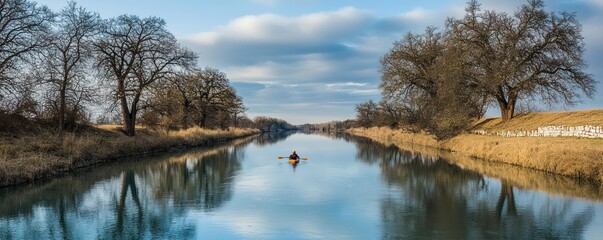 Obraz premium A serene river scene with a person kayaking amidst trees and reflections on the water.