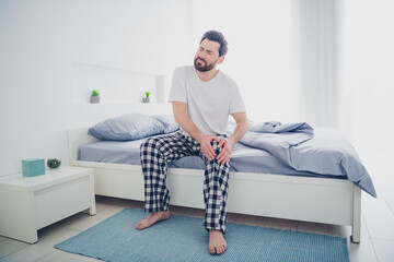 Photo of unhappy sad mature guy sleepwear pajama sitting bed having knee pain indoors home house...