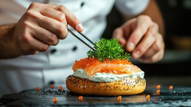 front view close up of a chef preparing a bagel with smoked salmon, cream cheese and caviar, we see him placing a very small parsely leaf with his chef