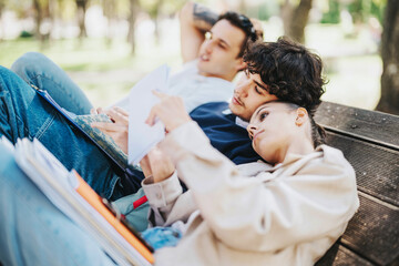 A group of relaxed students studying together on a park bench, enjoying a sunny day outdoors,...