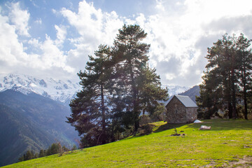 A small house sits atop a grassy hill in the mountains