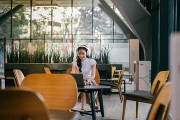 Young asian freelancer smiling and working on laptop in modern coworking space, wearing headphones...