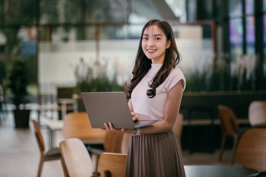 Smiling businesswoman holding a laptop, enjoying flexible working in a modern co-working space, showcasing the benefits of remote work and the digital nomad lifestyle