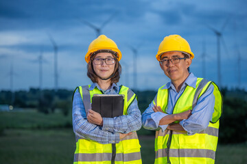 Two workers in safety vests stand in front of a wind farm