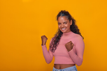 Young Indian woman stands confidently with her fists raised in triumph. Her bright smile...