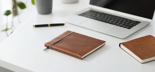 Brown leather notebooks and pen on white desk with laptop.