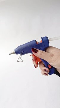 A woman's hand presses the button of the glue gun. Hot glue gun with rods.