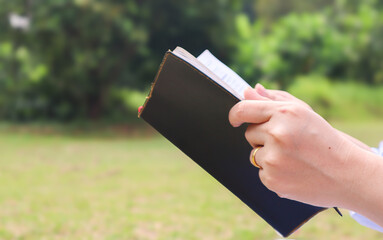 Cropped view of Asian woman's hands holding an open book relaxing in a park in the summer. Relax, lifestyle concept. Summer relaxation concept. Healthy lifestyle