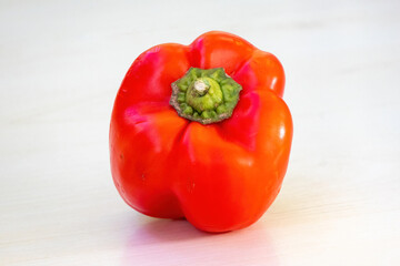 A vibrant ripe red bell pepper displayed on a light wooden surface. This versatile vegetable, also known as capsicum, red pepper, chili pepper, sweet pepper, jalapeno, cayenne, or paprika.