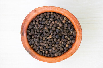 A top-down view of a clay cup filled with black peppercorns.