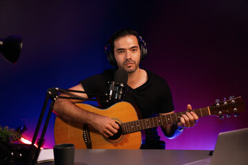 Obraz premium Host channel of smart influencer in creative audio on live streaming to fanclub with sing with play guitar music blogger using headset and mic social media online at neon light modern studio. Surmise.