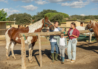 Young man, young woman and boy leads horse on tether to hitching post