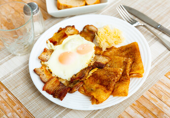 National german pancakes with pork meat, served with fried eggs, on a table in a cafe