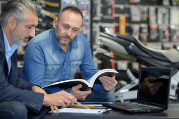 man and shop assistant in motorbike store checking a catalogue