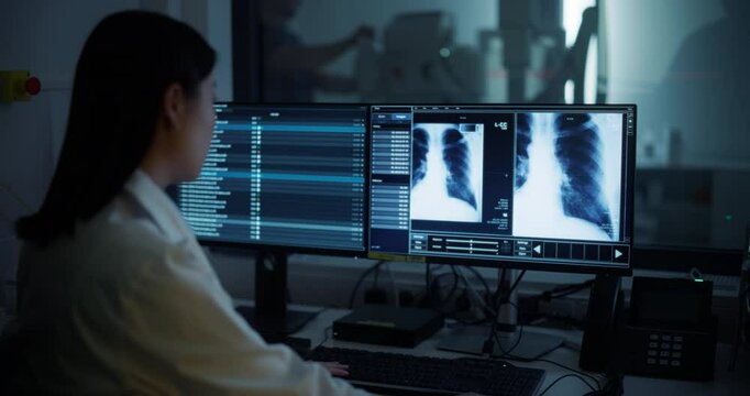 Radiologist Analyzing Chest X-rays on Multiple Monitors in a Dark Room. Male Nurse Assisting with Advanced Medical Equipment Visible in Background. Asian Female Doctor Focuses on Detailed Scans