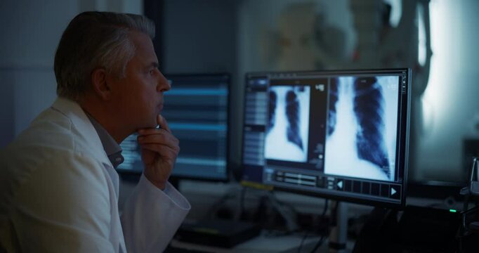 Experienced Radiographer Examines Chest X-rays on Multiple Computer Monitors in a Dark Medical Room. Modern Diagnostic Equipment Ready to Take Medical Imaging Scans of a Male Patient
