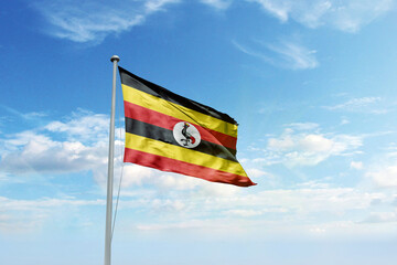 Waving flag of Uganda in blue sky. Uganda flag for Republic Day and Independence Day.