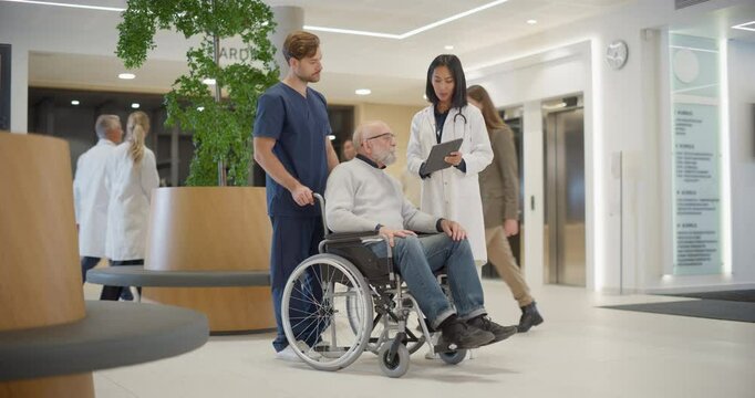 Asian Female Doctor Meeting a Senior Male Patient in a Wheelchair. Visitor is Assisted by a Male Nurse. Physician Using Tablet Computer to Show Medical Information and Test Results to the Elderly Man