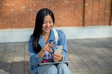 A female college student sits on the edge of a footpath at her university, using her smartphone.