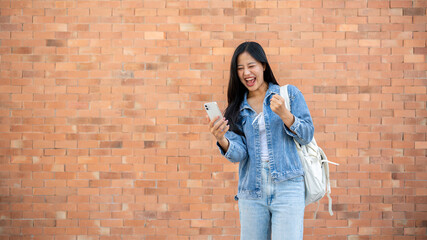 A cheerful Asian female college student shows a victory fist, receiving good news through a message.