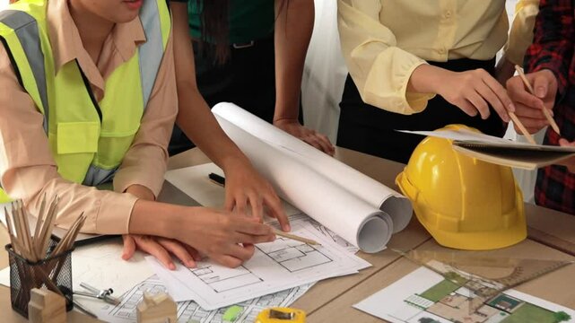 Smart architect and safety engineer discussion about building blueprint on table with architectural document, measurement tools and wooden block scatter around at modern office. Closeup. Delineation.