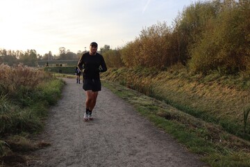 Obraz premium A trail runner, lit by the sun from behind, sticks out his tongue on a trail in autumn weather.