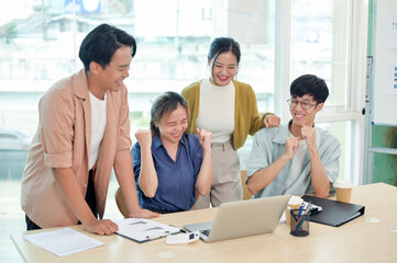 A cheerful young adult Asian business startup team celebrates their good news together.