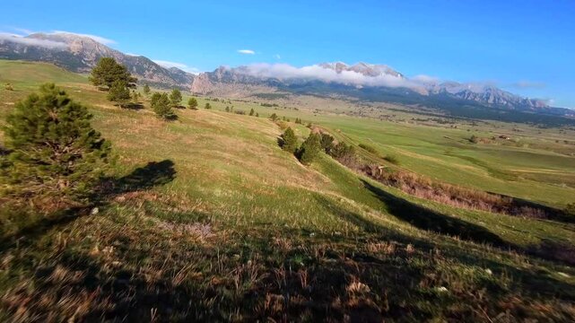 Low FPV drone footage gliding over a green open field and trail in Boulder, Colorado, with the iconic Flatirons shrouded in fog and low clouds in the distance