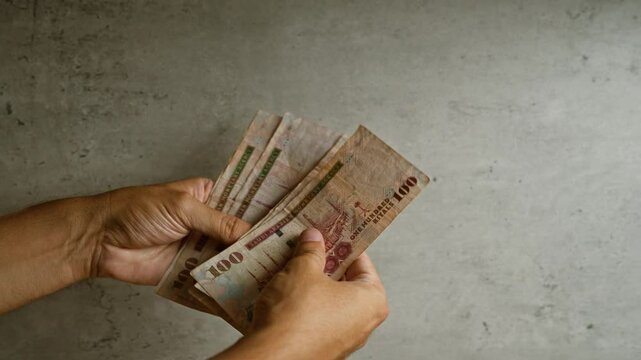 Man holding multiple saudi arabian riyals against a concrete background, showcasing a detailed view of the currency and hands handling money.