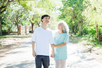 Naklejka premium A happy senior mother embraces her smiling adult son in a lush green park. Surrounded by nature, their affectionate hug symbolizes love, peace, vitality, and renewal under the serene greenery