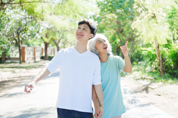 Obraz premium A happy senior mother embraces her smiling adult son in a lush green park. Surrounded by nature, their affectionate hug symbolizes love, peace, vitality, and renewal under the serene greenery