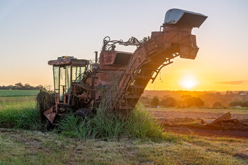 Old sugar cane harvester machinery in paddock, sunset on farm, agricultural scene landscape