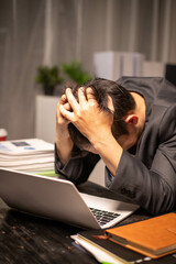 A man works overtime at his desk in the office of the office to clear documents to send to the customer. During work, he is stressed from work and happy after finishing the work for the customer.