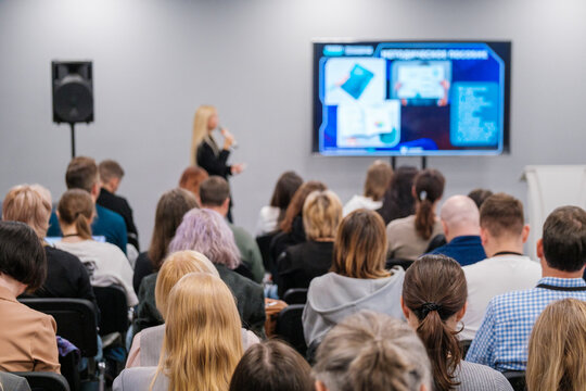 Diverse audience attentively listening to a speaker at a business conference. Presentation displayed on a big screen in a modern meeting room setting.
