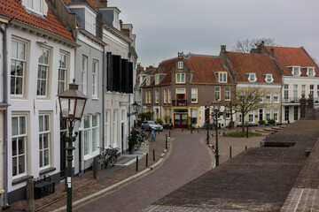 Fototapeta premium A quiet European street, charming historic houses, red-tiled roofs, and cobblestone paving. Lanterns line the street, adding a timeless atmosphere under an overcast sky. Wijk bij Duurstede landscape