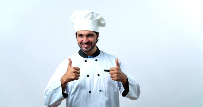 Portrait of Indian Asian Young Confident Male Chef or Professional Cook in White Coat and Hat Giving Thumbs Up Sign for Excellence While Standing Against White Background