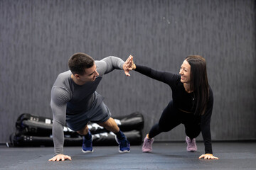 A man and woman high-five while maintaining a plank position together, showcasing their advanced teamwork and coordination skills during a gym workout session.