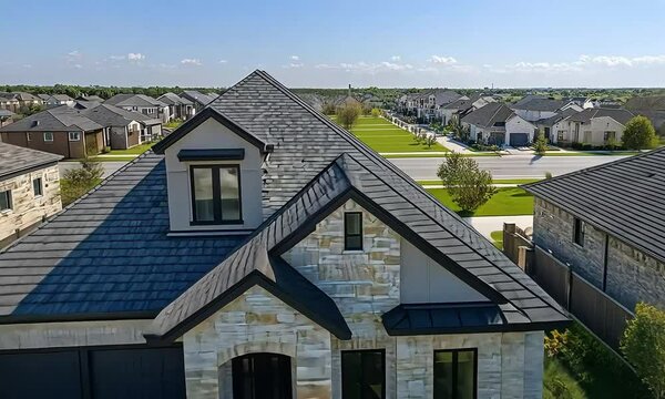 Elegant stone house with black roof and garage, featuring well-maintained landscaping and a paved driveway, surrounded by similar homes