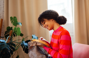 A smiling young African woman in a red sweater is embroidering while sitting in an armchair