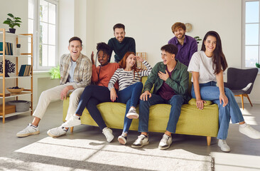 Diverse group of multinational people, friends, and colleagues gathers on a sofa, sharing smiles, laughter, and engaging conversations. Group portrait of positive young people at home.