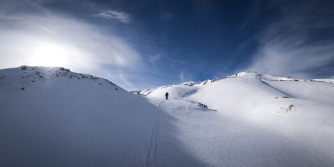Ski touring in the Beaufortain in the French alps. Skier in the fresh snow with blue sky and sun.