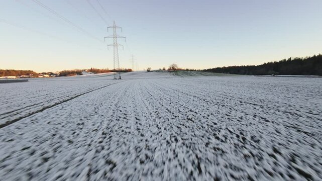 Aerial FPV of sunrise over snowy fields and forest, crisp winter air and golden sunlight underneath electricity towers