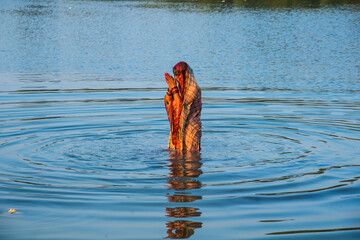 Traditionally dressed Indian woman pray into the river on Chhat Puja Festival.