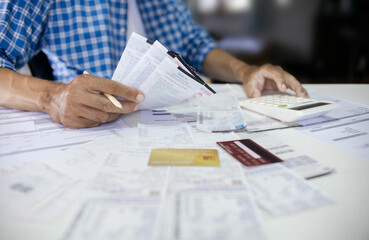 Asian man sitting at desk holding receipt of expenses and calculate all loan bills and try to find...