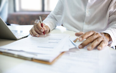 Asian businessman reviewing document reports at office workplace with computer laptop. legal expert, professional lawyer reading and checking financial documents or insurance contract