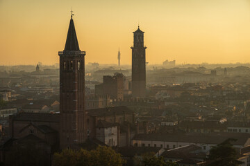 A stunning view of Verona at sunset, showcasing historic towers and a sprawling cityscape under a warm, golden sky.
